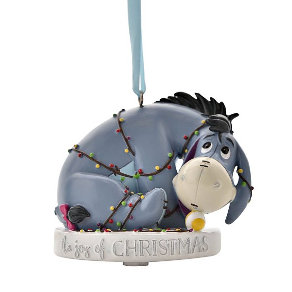 A polyresin Christmas tree decoration depicting Eyeore from Disney's Winnie the Pooh tangled up in a string of festive lights. He sits upon a white plinth that has silver text around it that reads 'The joy of Christmas' and hangs from a silver ribbon.