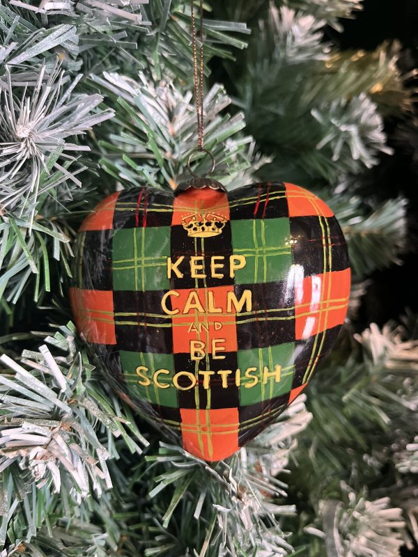 This hand painted Heart shaped glass Christmas bauble features a background of red and green tartan with the words "Keep Calm and be Scottish" on the front in gold beneath a gold crown. A twist on the iconic Ministry of Information posters of wartime Britain.These baubles bring a lovely touch of Scotland to your Christmas Tree or a thoughtful gift for a far-from-home Scot!