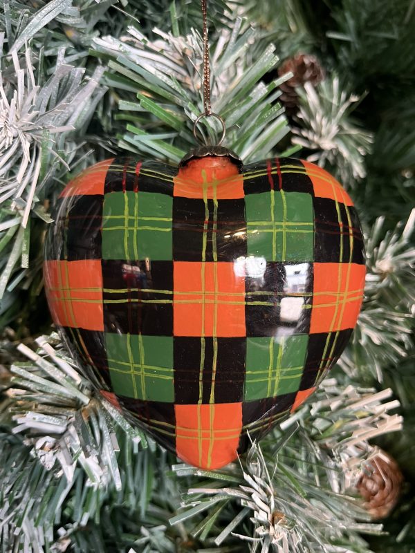 A Hand Painted Heart Shaped Glass Christmas Bauble painted to look like tartan in black, green and red with gold deatil hanging on a Christmas tree.