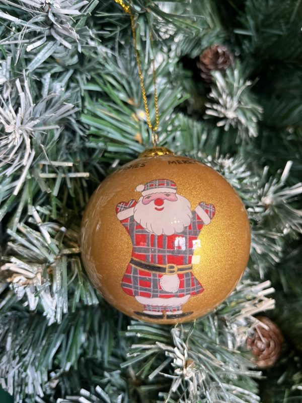 A gold glass Christmas tree bauble decorated with a hand painted Cheerful Tartan Clad Santa Claus wearing a kilt and sporran hanging on a Christmas tree.