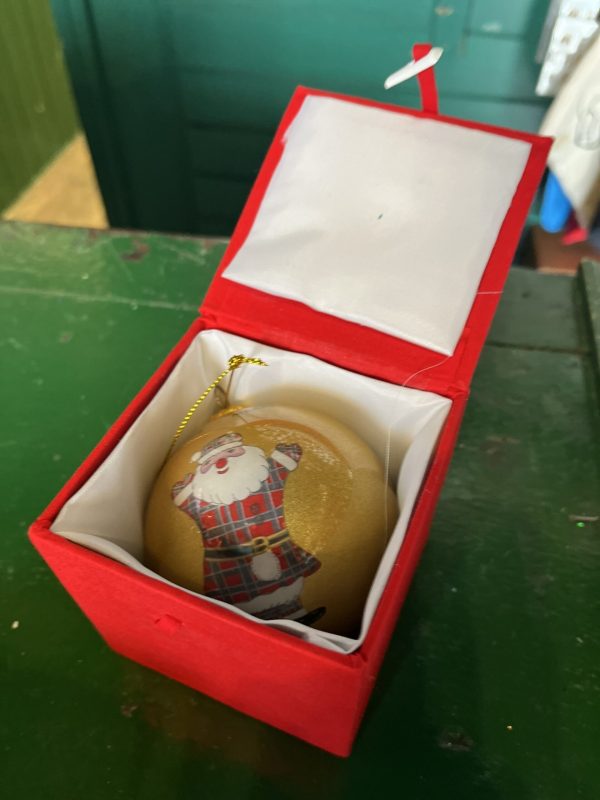 A Christmas decoration of Hand Painted Gold Scottish Santa Glass Christmas Bauble depicted as a Scottish golfer, presented in an open red gift box.