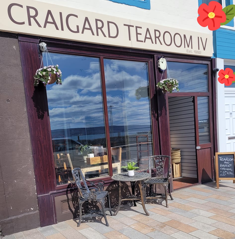 A tearoom with the sign "CRAIGARD TEAROOM IV" and "Est. 1922" above its entrance. There are two metal chairs and a small table with a plant in front of the large window.