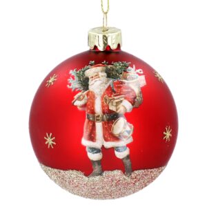 A decorative red Christmas ornament features a traditiomal looking Santa Claus with a sack of gifts over his shoilder and holding a drum, embellished with gold glitter snowflakes with a gold glitter base.